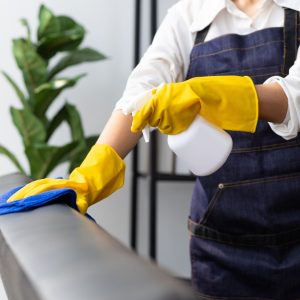A house cleaner wearing an apron uses a cloth to clean the sofa in the house. Wipe dust from the house.